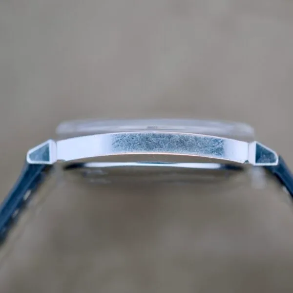 Side view of a Benrus Automatic Sea Lord Date case showing visible scratches on the metal, paired with a dark strap against a blurred beige background.