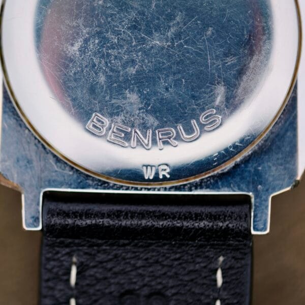 Close-up of the back of a Benrus Automatic Sea Lord Date wristwatch with BENRUS and WR engraved on the metal case, featuring a black leather strap with white stitching.