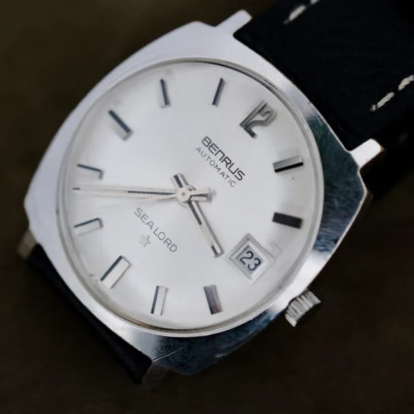 A close-up of a Benrus Automatic Sea Lord Date wristwatch with a silver dial, black hour markers, date at 23, and black leather strap. The time shown is about 8:42:36.