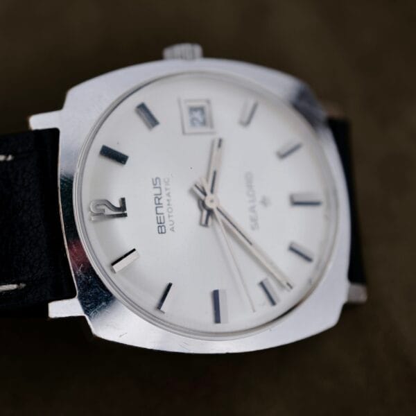 A close-up of a Benrus Automatic Sea Lord Date wristwatch with a white dial, black hour markers, black hands, date window at 3 o’clock, and a black leather strap. The watch is angled slightly to the left.