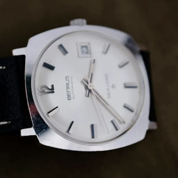 A close-up of a Benrus Automatic Sea Lord Date wristwatch with a white dial, black hour markers, black hands, date window at 3 o’clock, and a black leather strap. The watch is angled slightly to the left.