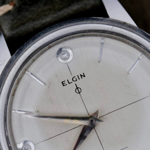Close-up of the Elgin 19 Jewels Manual Wind Diamond Indices wristwatch face, showing silver hands and markers, diamond indices, fine quadrant lines, and the ELGIN name centered on a white background.