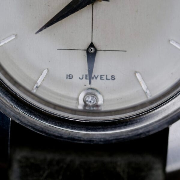 Close-up of the Elgin 19 Jewels Manual Wind Diamond Indicies watch face, featuring 19 JEWELS, diamond hour markers, and hands near 6 oclock in a simple, round metal case.