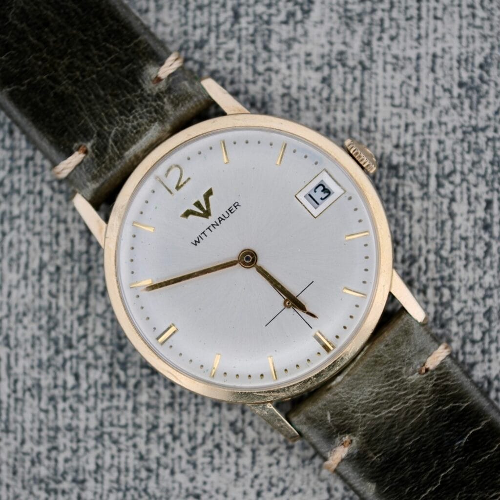 A Wittnauer Date Manual Wind 2732-1-C189 wristwatch featuring a leather strap, manual wind movement, and date display showing the 13th.