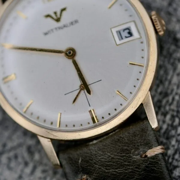 A close-up of the Wittnauer Date Manual Wind 2732-1-C189 wristwatch shows a white and gold dial, gold markers, date display at 13, black leather strap, and the time reading about 6:01:27.