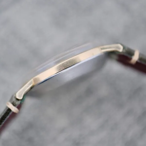 A close-up side view of the Wittnauer Date Manual Wind 2732-1-C189, highlighting its metal case and leather strap at the edge and lugs, set against a textured gray background. The watch face is not shown.