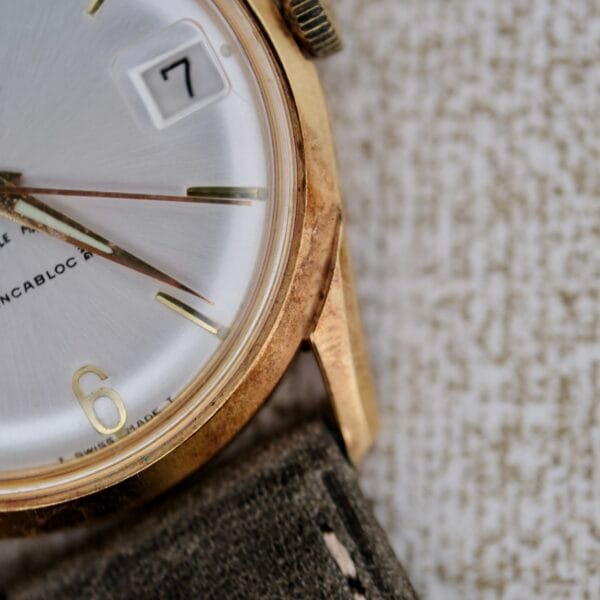 Close-up of a Truway 17 Jewels Date Incabloc wristwatch featuring a gold case, white dial with date window set to 7, green fabric strap, and partial INCABLOC text visible on the face.