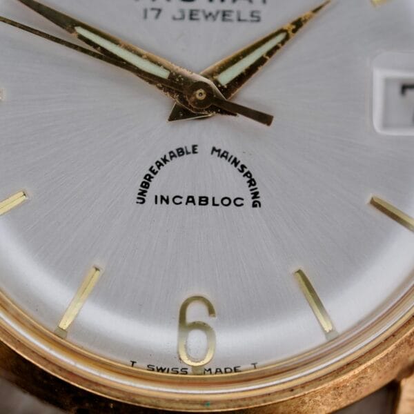 Close-up of a vintage Truway 17 Jewels Date Incabloc watch face with gold hands, gold hour markers, “UNBREAKABLE MAINSPRING INCABLOC” text, the number 6, and “T SWISS MADE T” visible at the bottom.