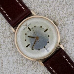 Wittnauer 627-1-215 Manual Wind Date wristwatch with a brown leather strap and date display, displayed on a textured surface.
