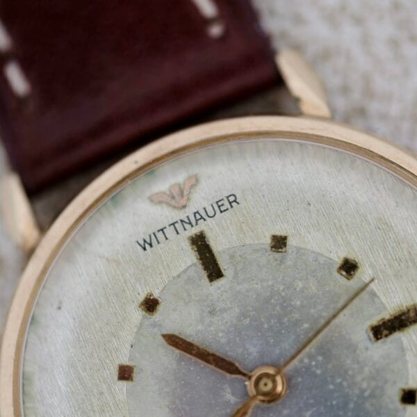 Close-up of a Wittnauer 627-1-215 Manual Wind Date wristwatch with a worn, scratched face, gold hour markers and hands, brown leather strap, and the Wittnauer logo visible near the top.