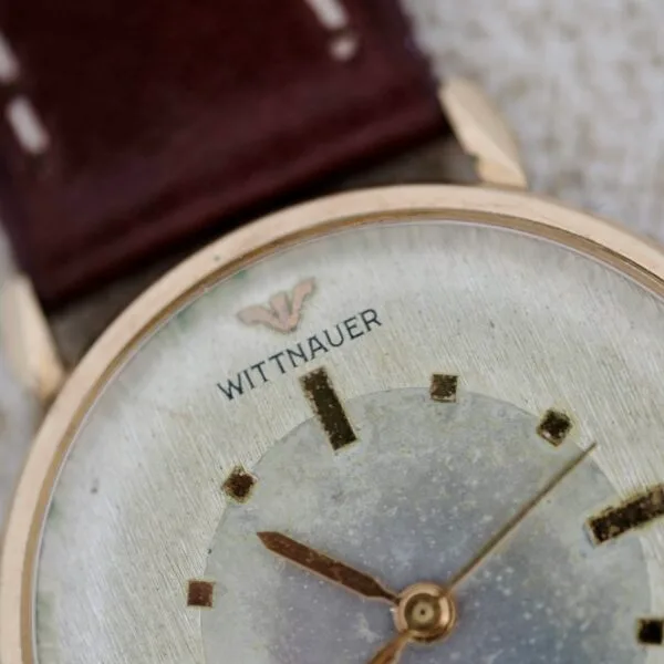 Close-up of a Wittnauer 627-1-215 Manual Wind Date wristwatch with a worn, scratched face, gold hour markers and hands, brown leather strap, and the Wittnauer logo visible near the top.