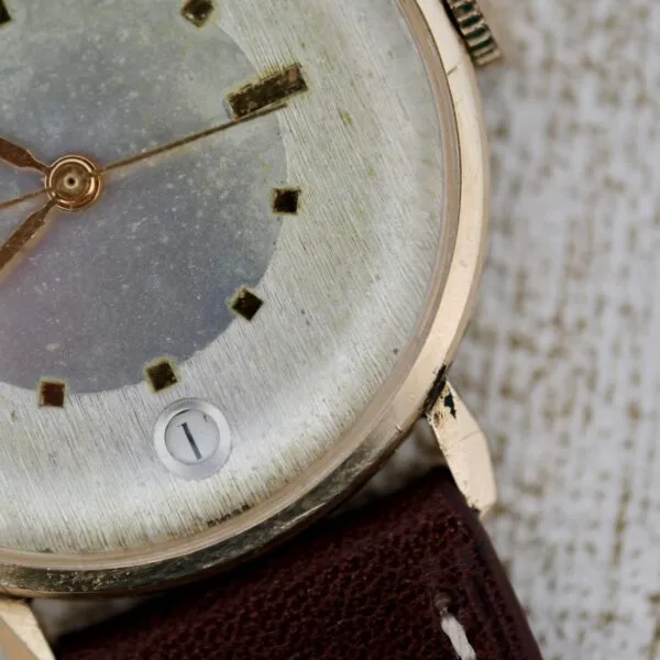 A close-up of a Wittnauer 627-1-215 Manual Wind Date wristwatch features a worn gold case, brown leather strap, square hour markers, gold hands, and a date window showing 1 on the aged watch face.