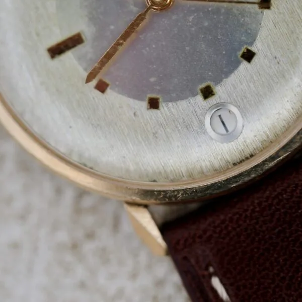Close-up of a Wittnauer 627-1-215 Manual Wind Date with a weathered face, square hour markers, brown leather strap, date display showing the 1st, and the time at 1:36.