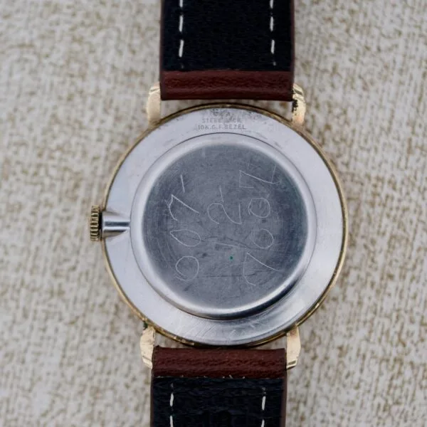 A close-up of the back of a Wittnauer 627-1-215 Manual Wind Date wristwatch with a brown leather strap. The scratched metal case features markings and engravings, including 1969 and faint engraving near the top edge.