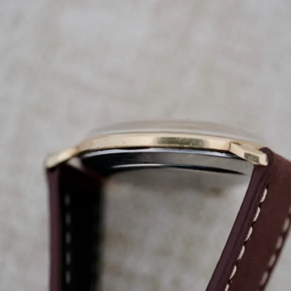 Close-up side view of the Wittnauer 627-1-215 Manual Wind Date wristwatch featuring a brown leather strap with white stitching, gold-tone bezel, and slightly domed glass set against a softly blurred background.