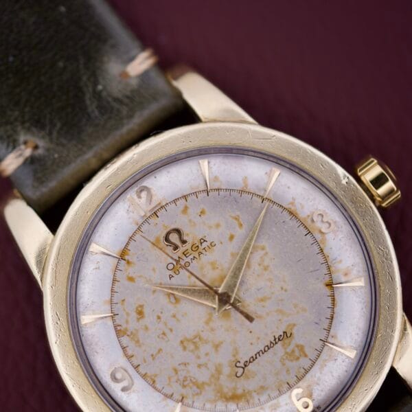 Close-up of the Omega Seamaster Automatic 2577-17 with a worn Tropic Dial and dark leather strap, set against a maroon background.