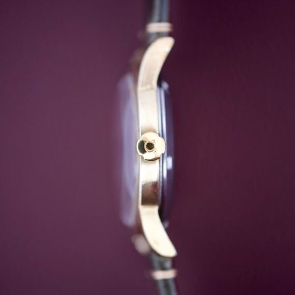 Side view of the Omega Seamaster Automatic 2577-17 Tropic Dial gold wristwatch with a round crown, set against a solid maroon background.