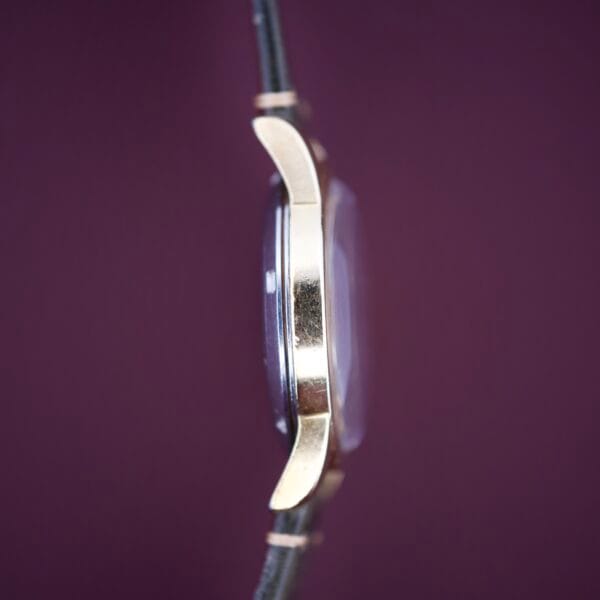 Side view of an Omega Seamaster Automatic 2577-17 Tropic Dial gold wristwatch with a black strap, set against a purple background.