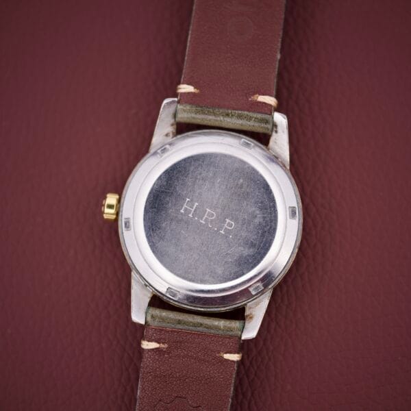 An Omega Seamaster Automatic 2577-17 Tropic Dial wristwatch with a brown leather strap and H.P.P. engraved on the metal back, displayed on a maroon surface.