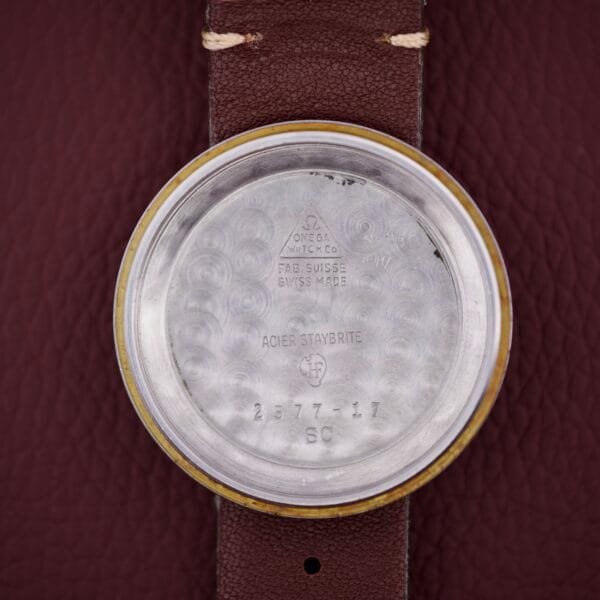 The inside case back of an Omega Seamaster Automatic 2577-17 Tropic Dial features engraved text and numbers, resting on brown leather—an intriguing detail for any Automatic timepiece enthusiast.