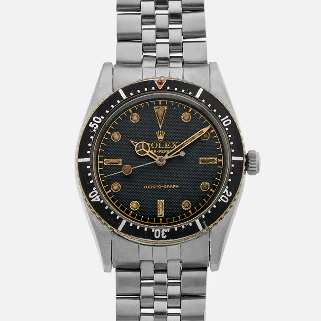 A vintage Rolex Turn-O-Graph 6202 wristwatch with a black rotating bezel, black dial, gold hour markers, and a silver metal link bracelet is shown against a white background.