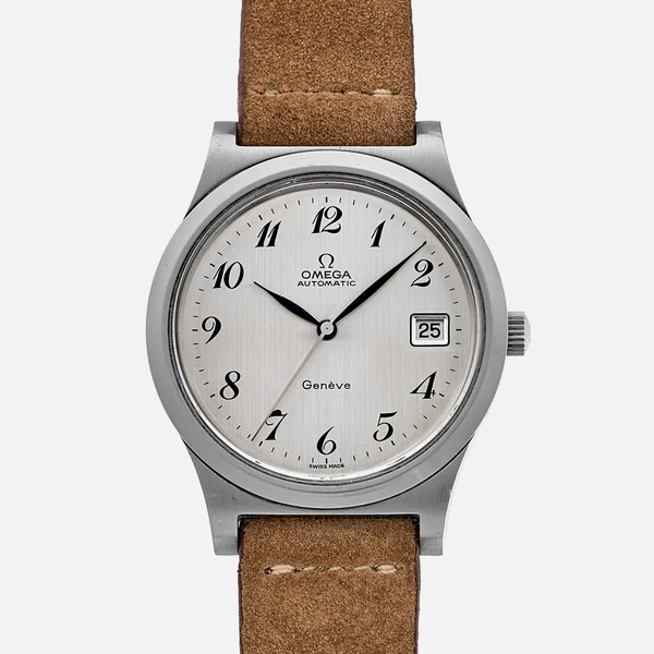 A silver Omega Genève automatic wristwatch with a brown suede strap, black Arabic numerals, a date window at 3 o’clock, and silver hour and minute hands on a white textured dial.