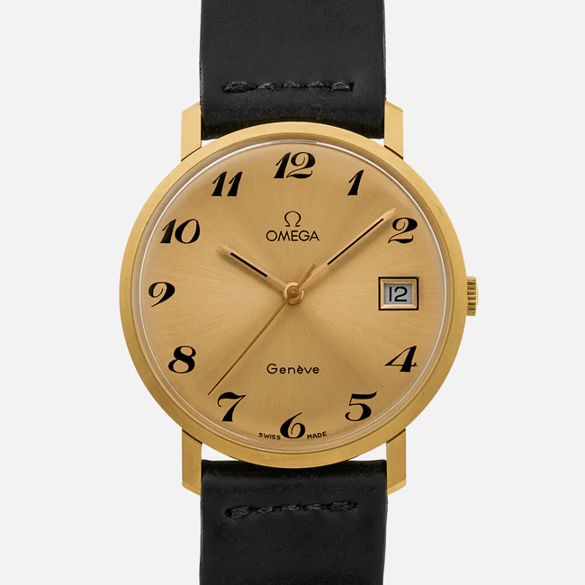 A gold Omega Genève wristwatch with a round dial, black numerals, a date window at 3 oclock, and black leather strap. The hour, minute, and second hands are gold. The face has Omega, Genève, and Swiss Made text.