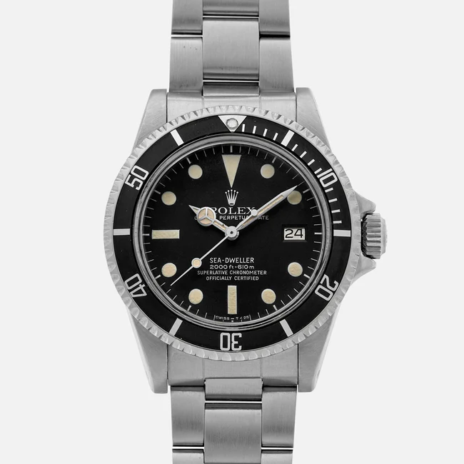 A stainless steel Rolex Sea-Dweller 1665 watch with a black dial, luminous hour markers, date window at 3 o’clock, and a rotating bezel, shown on a metal bracelet against a plain background.