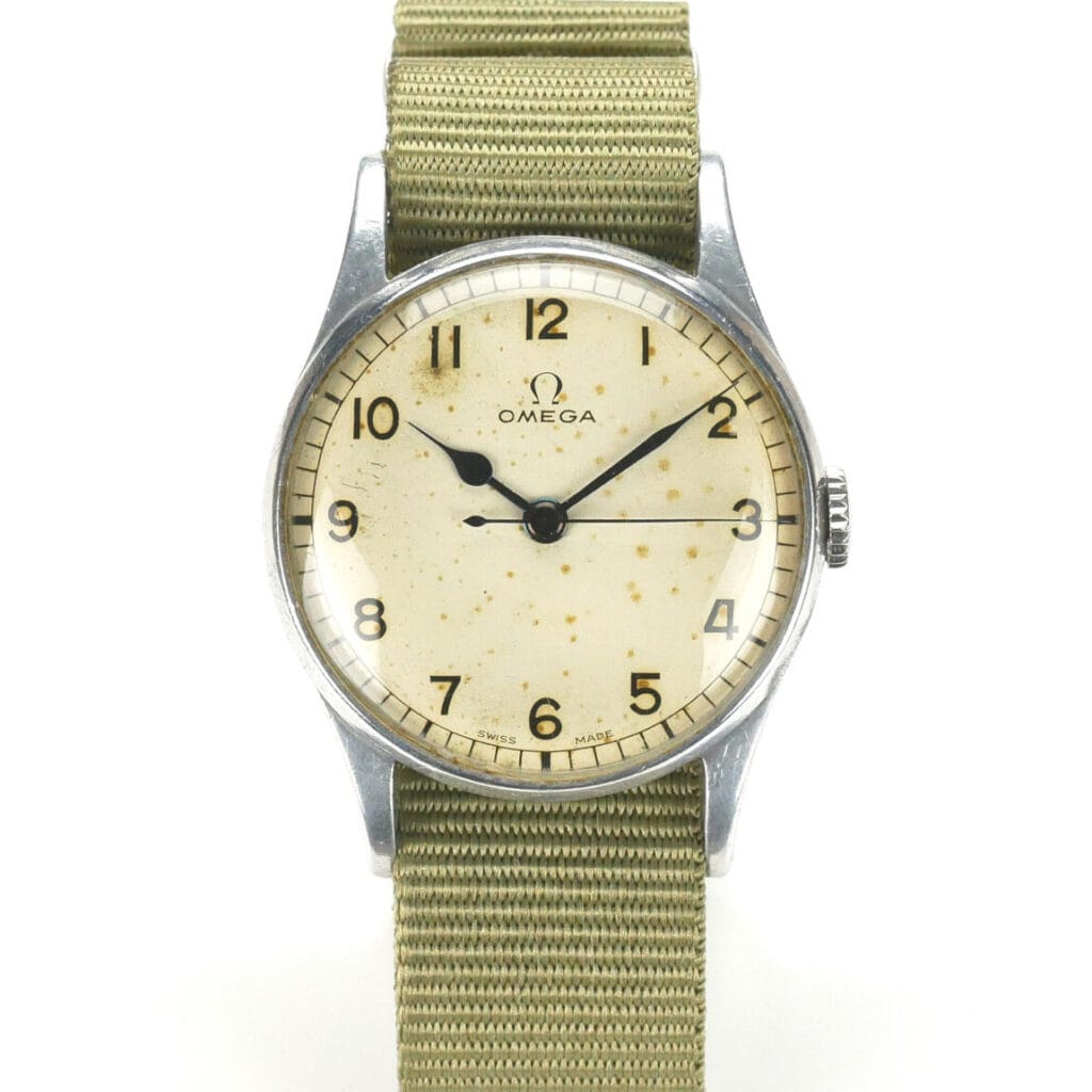A vintage Omega 6B/159 1943 Issue wristwatch featuring a round, off-white dial with patina, bold black numerals, and two hands in a silver case, paired with a textured khaki fabric strap. The Omega logo sits below the 12 o’clock position.