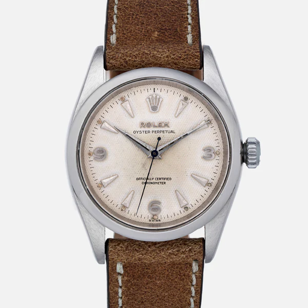 A vintage Rolex Oyster Perpetual 6580 watch featuring a brown leather strap and a classic cream dial.