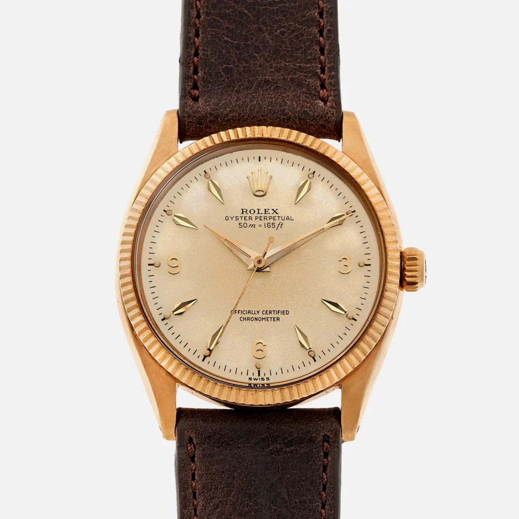 A vintage gold Rolex Oyster Perpetual wristwatch with a brown leather strap and a champagne-colored dial, model 6567.