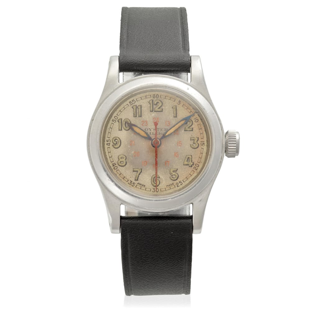 A vintage Rolex wristwatch with a worn beige dial, black leather strap, silver case, and classic Oyster design.