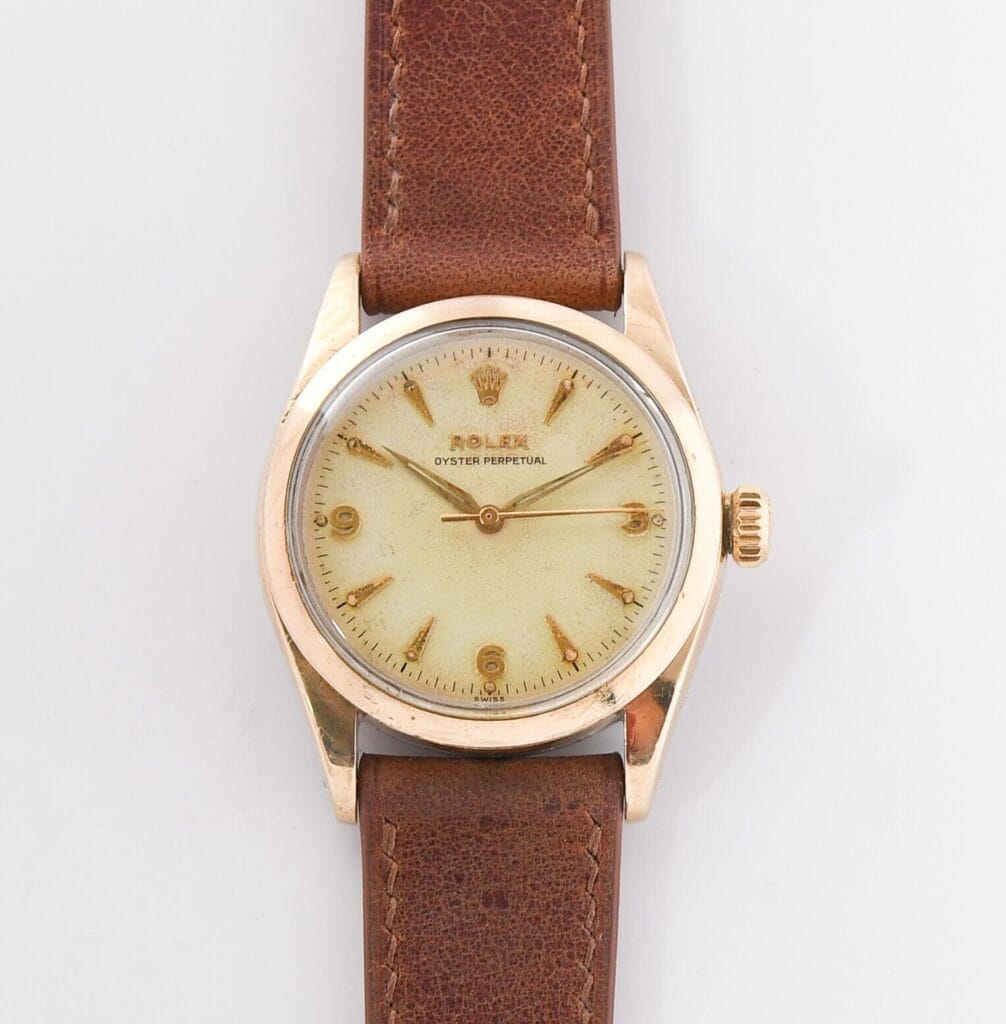 A vintage Rolex Oyster Perpetual 6334 wristwatch with a brown leather strap and a gold case on a white background.