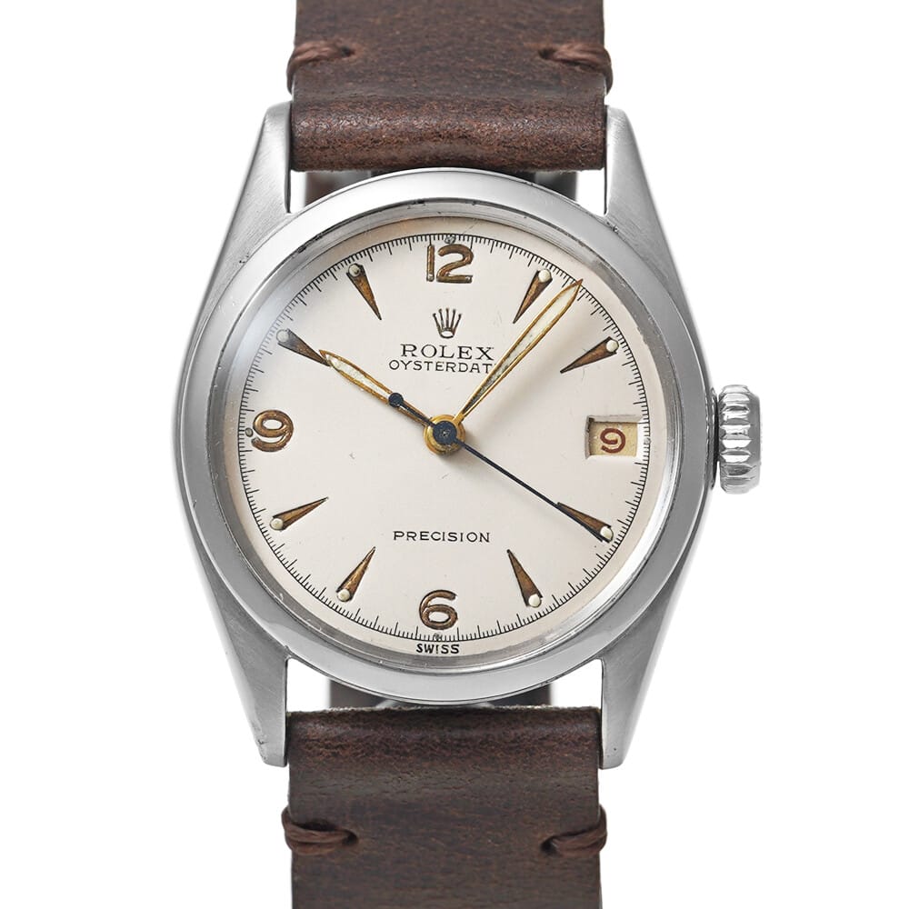 A vintage Rolex Oysterdate wristwatch with a brown leather strap and silver dial displays the time 4:41:36, showcasing the classic style of a Precision 6066.