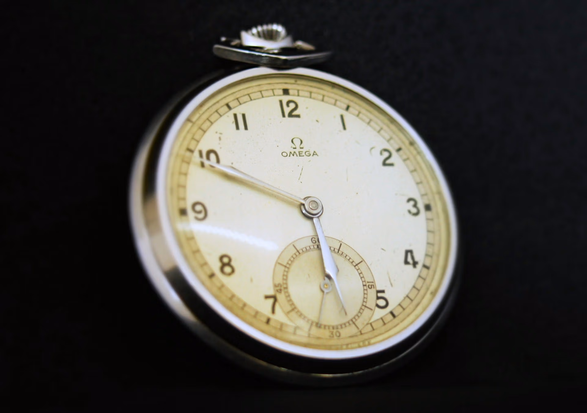 Close-up of a vintage Omega pocket watch with a white face and black numerals, featuring an engraved omega reference number, set against a dark background.