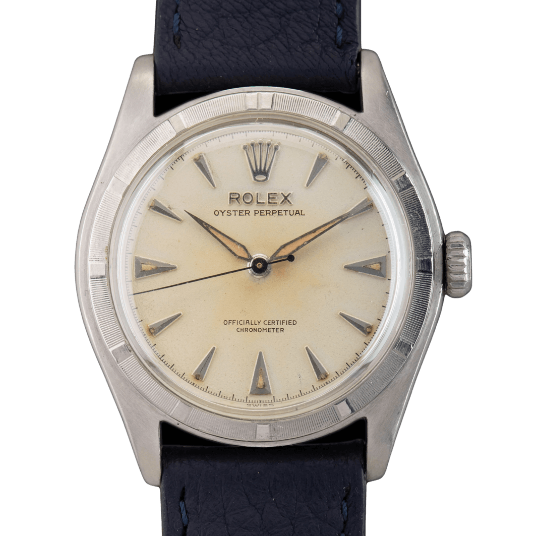 A vintage Rolex Oyster Perpetual 6107 watch featuring a cream dial and black leather strap.