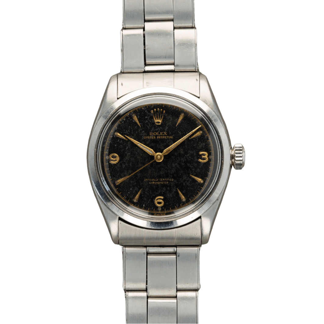 A vintage Rolex Oyster Perpetual 6284 wristwatch with a black dial, gold markers, and a silver metal bracelet against a gray background.