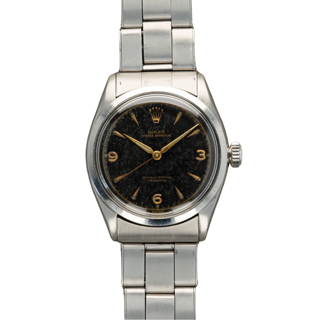 A vintage Rolex Oyster Perpetual 6284 wristwatch with a black dial, gold markers, and a silver metal bracelet against a gray background.