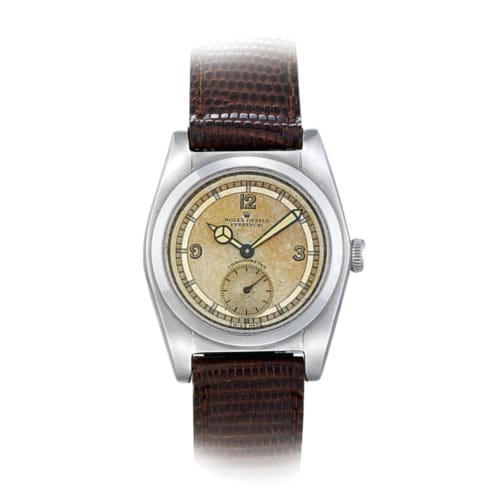A vintage Rolex Oyster Perpetual wristwatch with a brown leather strap and a beige dial showing hours, minutes, and seconds.