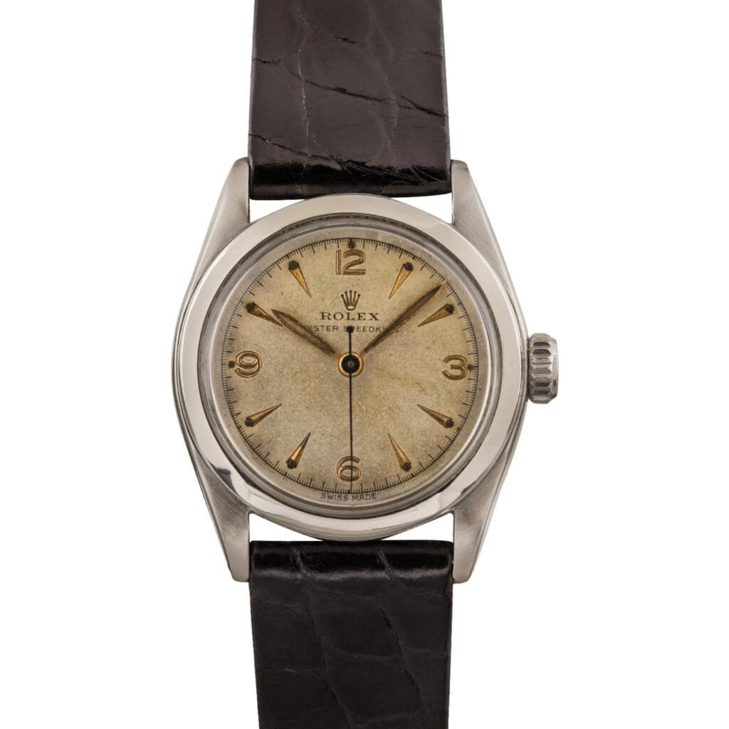 Vintage Rolex Oyster Speedking 6020 wristwatch with a cream-colored dial, gold hour markers, and a black leather strap.