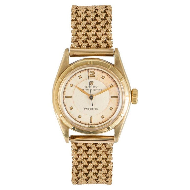 A vintage gold Rolex Oyster Speedking wristwatch with a woven beige and gold band, featuring a round cream dial.