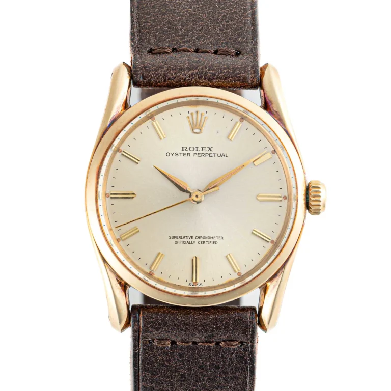 Gold Rolex Oyster Perpetual 1010 watch featuring a brown leather strap and a simple, silver dial.