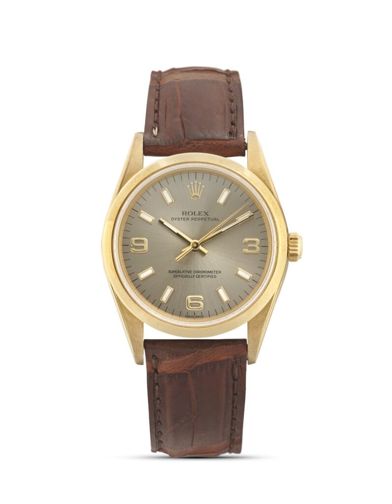 A gold Rolex Oyster Perpetual watch, model 14208, with a brown leather strap and a gray dial, elegantly displays the time at 10:09.