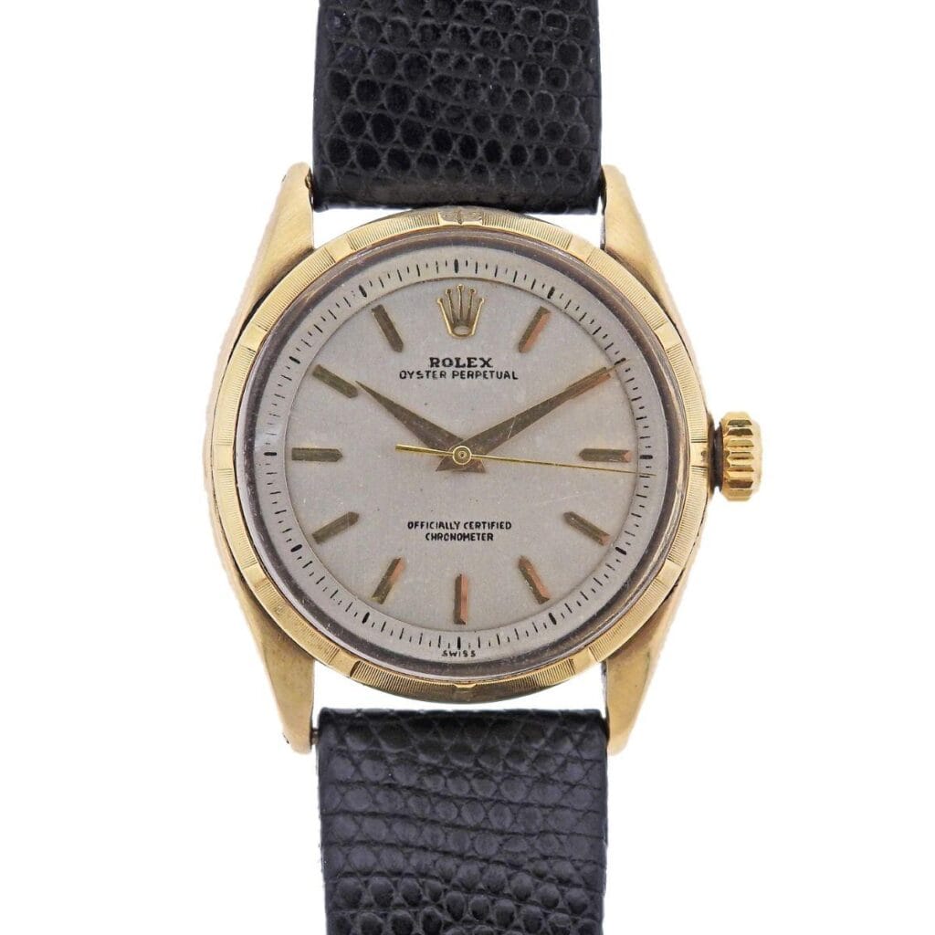 A vintage gold Rolex Oyster Perpetual 6585 watch featuring a black leather strap and a classic silver dial.