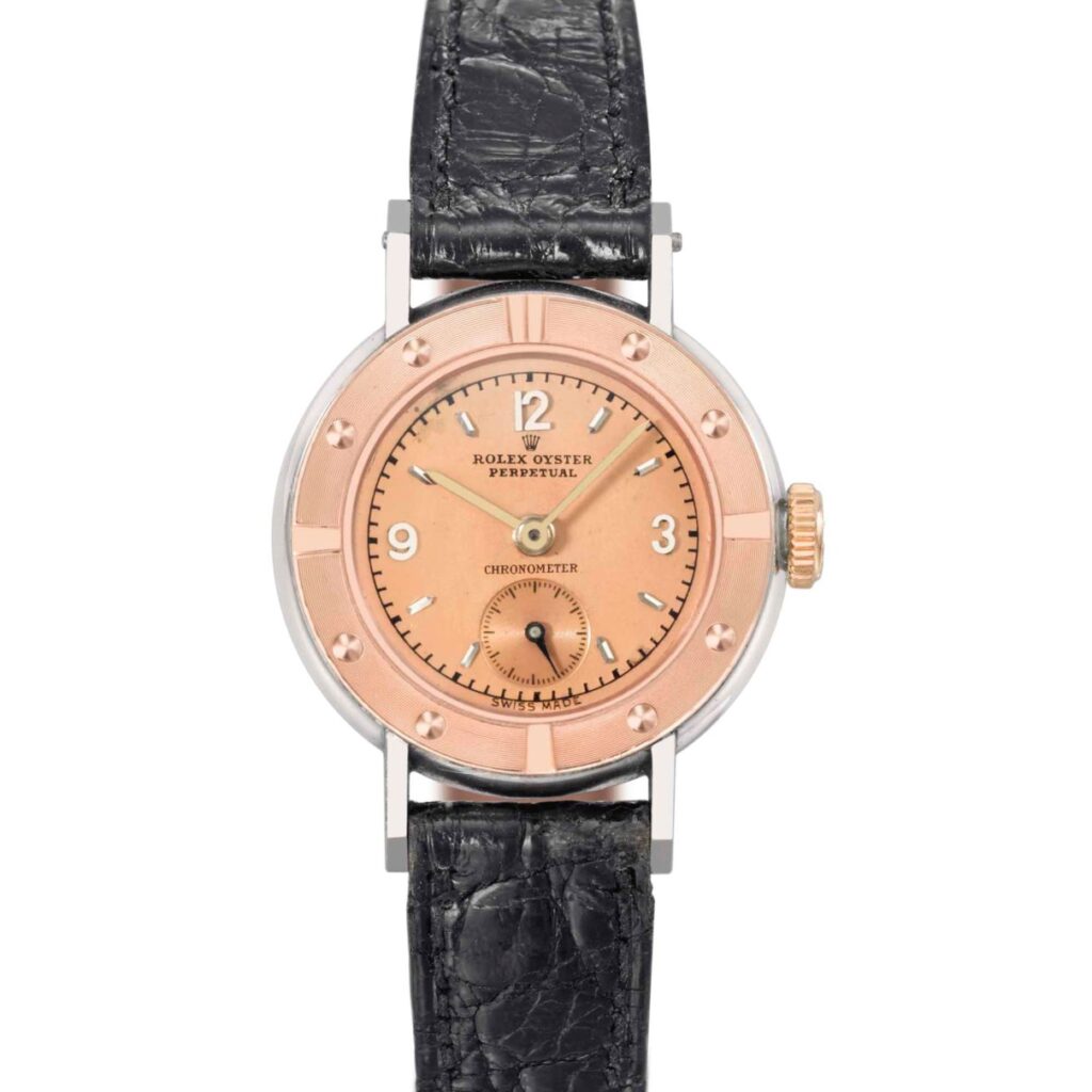 A vintage Rolex Oyster Perpetual wristwatch featuring a pink dial, black leather strap, and silver case.