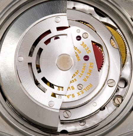 Close-up of a mechanical watch movement with gears and engraved text visible on metal parts.