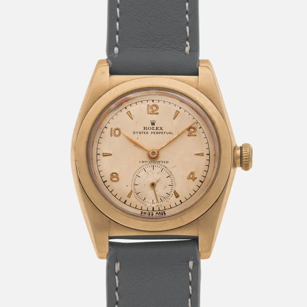 A vintage Rolex Oyster Perpetual wristwatch featuring a 3130 movement, gold case, cream dial, and dark leather strap.