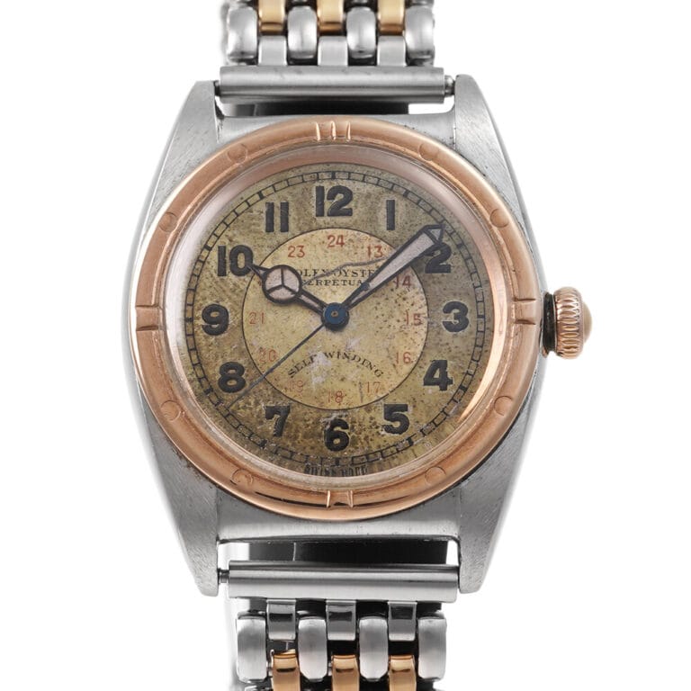 Vintage Rolex Oyster Perpetual wristwatch with a worn, tan dial, Arabic numerals, and a two-tone metal band.