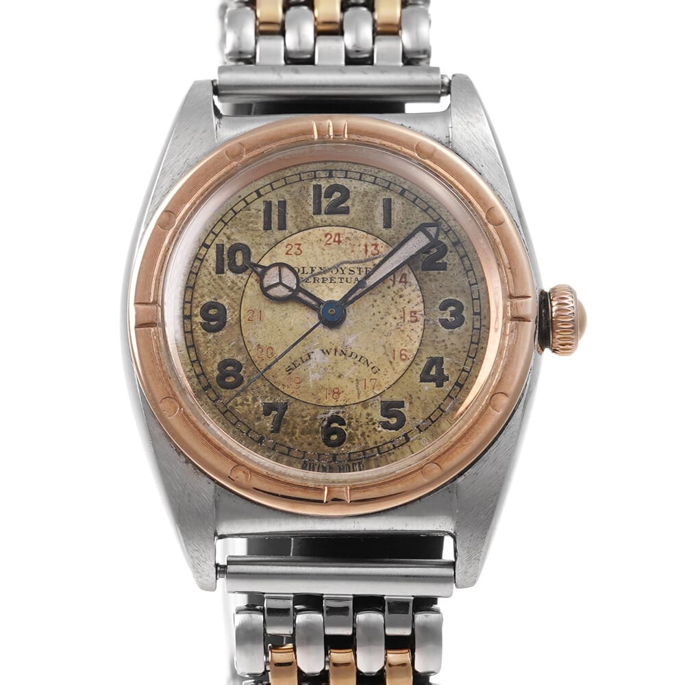 Vintage Rolex Oyster Perpetual wristwatch with a worn, tan dial, Arabic numerals, and a two-tone metal band.