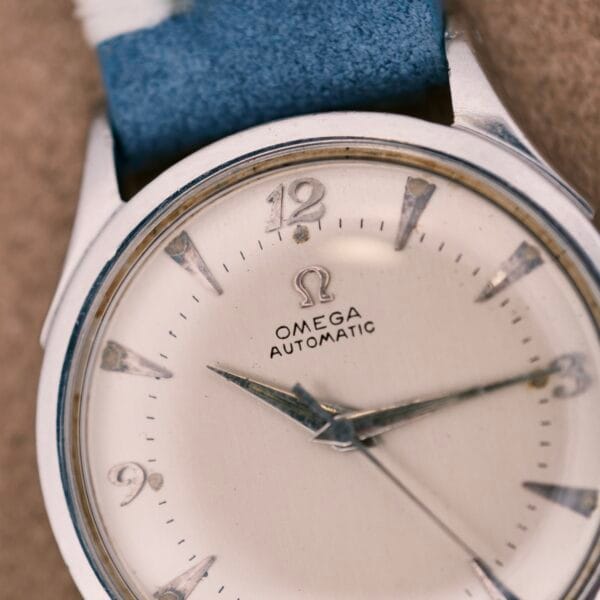 Close-up of an Omega Automatic Bumper 2635 Cal. 351 wristwatch, featuring a blue strap and silver hour markers.